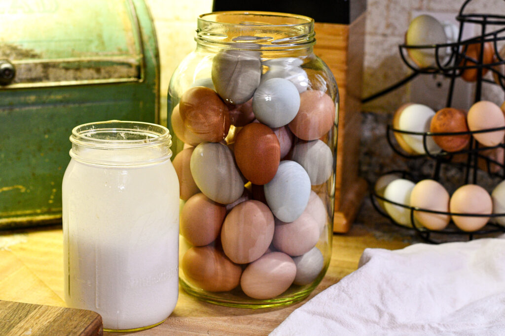 Picture of a quart jar of lime water sitting next to a gallon jar full of beautifully colored farm eggs