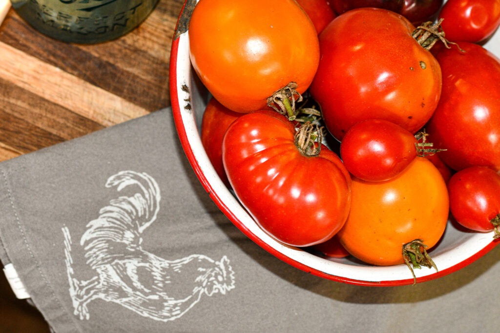 Tomatoes in a bowl sitting on a rooster kitchen towel
