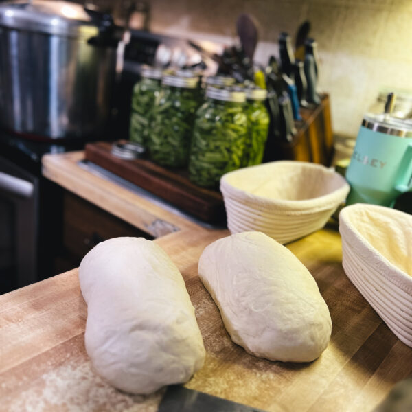 bread dough on a counter next to banneton baskets and quarts of green beans.